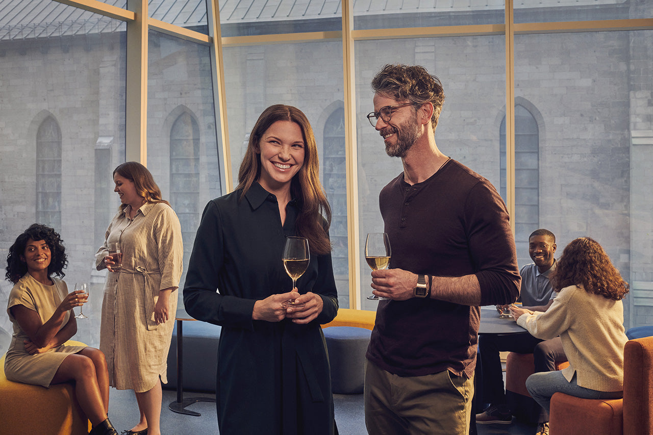 Personnes réunies dans un espace lounge vitré, échangeant autour d’un verre dans une ambiance conviviale.