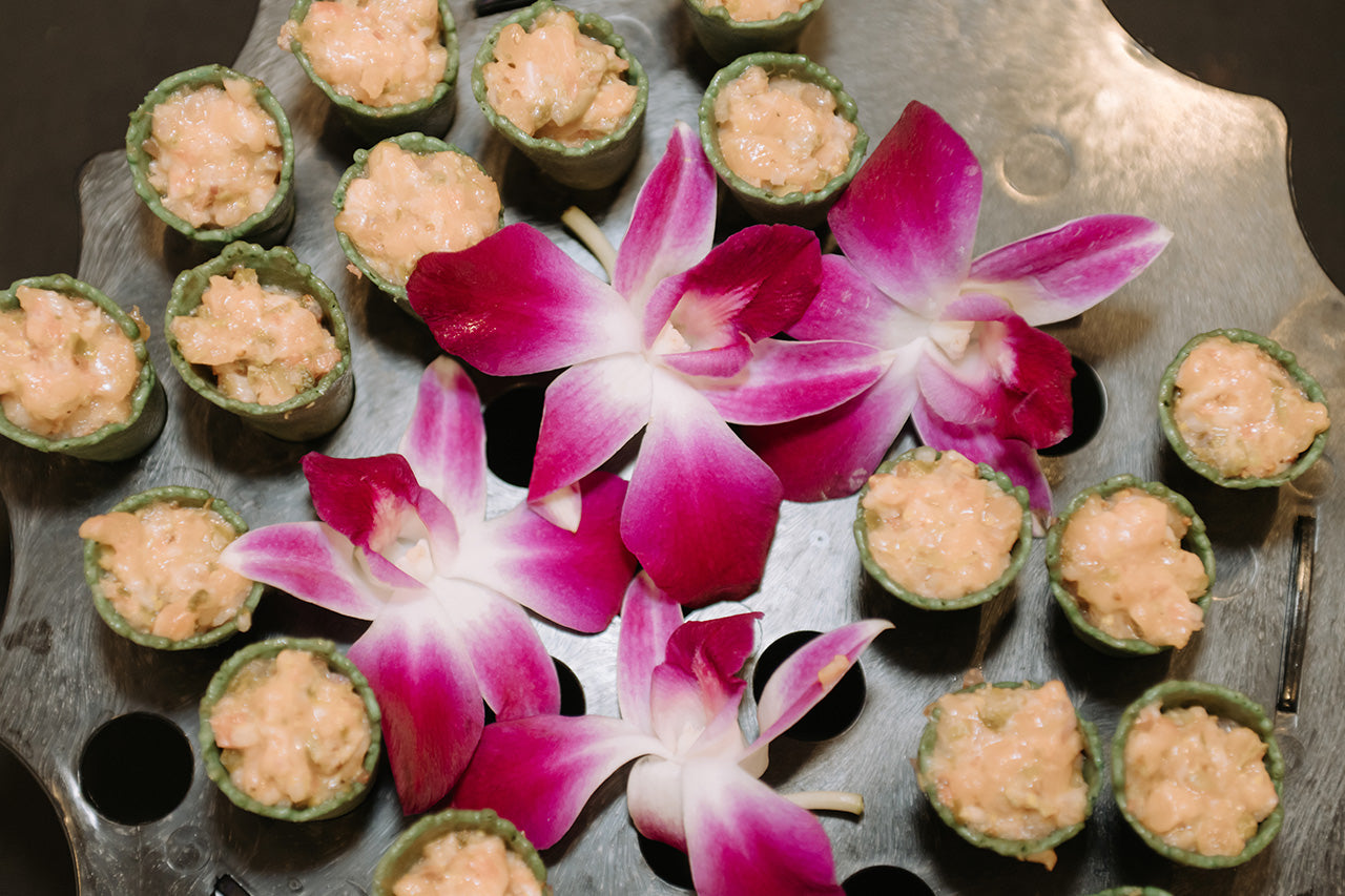 Bouchées apéritives disposées sur un plateau, agrémentées de fleurs orchidées aux teintes rose et blanc.